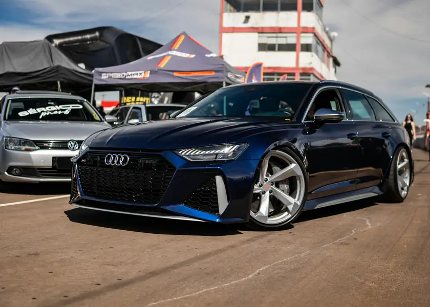 A blue Audi RS6 Avant in a track paddock beside race-day awnings