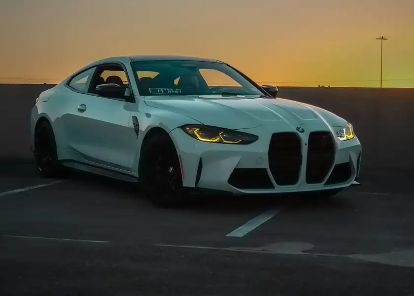 A white BMW M4 Competition parked on an open deck at sunset