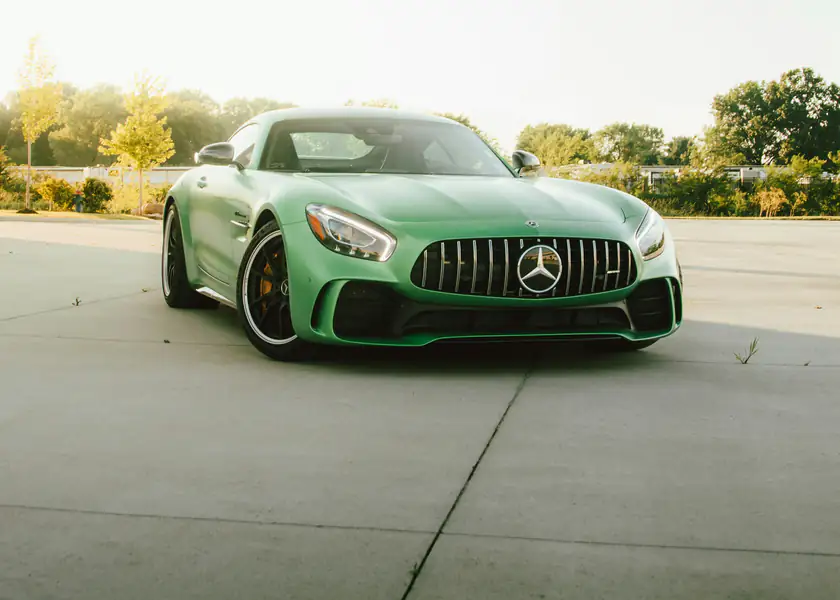 A green Mercedes-AMG GT parked on an open concrete pad in late afternoon light
